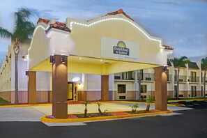 A hotel entrance with a sign for Days Inn & Suites, featuring a covered entrance area with pillars and a small garden. - Days Inn & Suites by Wyndham Tampa/Fairground/Casino Area (Tampa)
