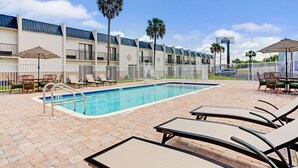 Un espace piscine d’hôtel comprenant des chaises longues, une piscine et une clôture.