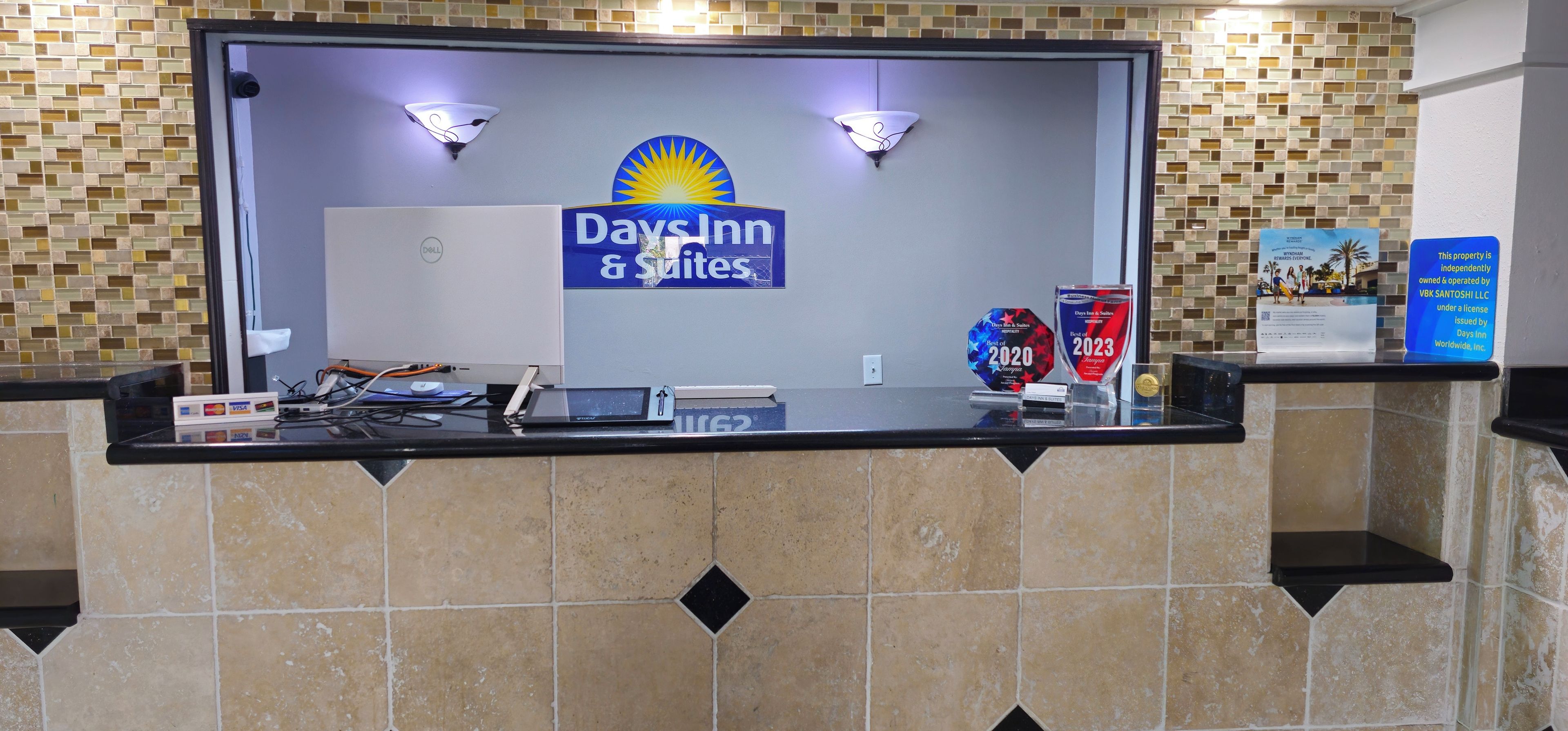 A reception desk with a Days Inn & Suites sign, a Dell computer, and a plaque for the Best of 2023 award.