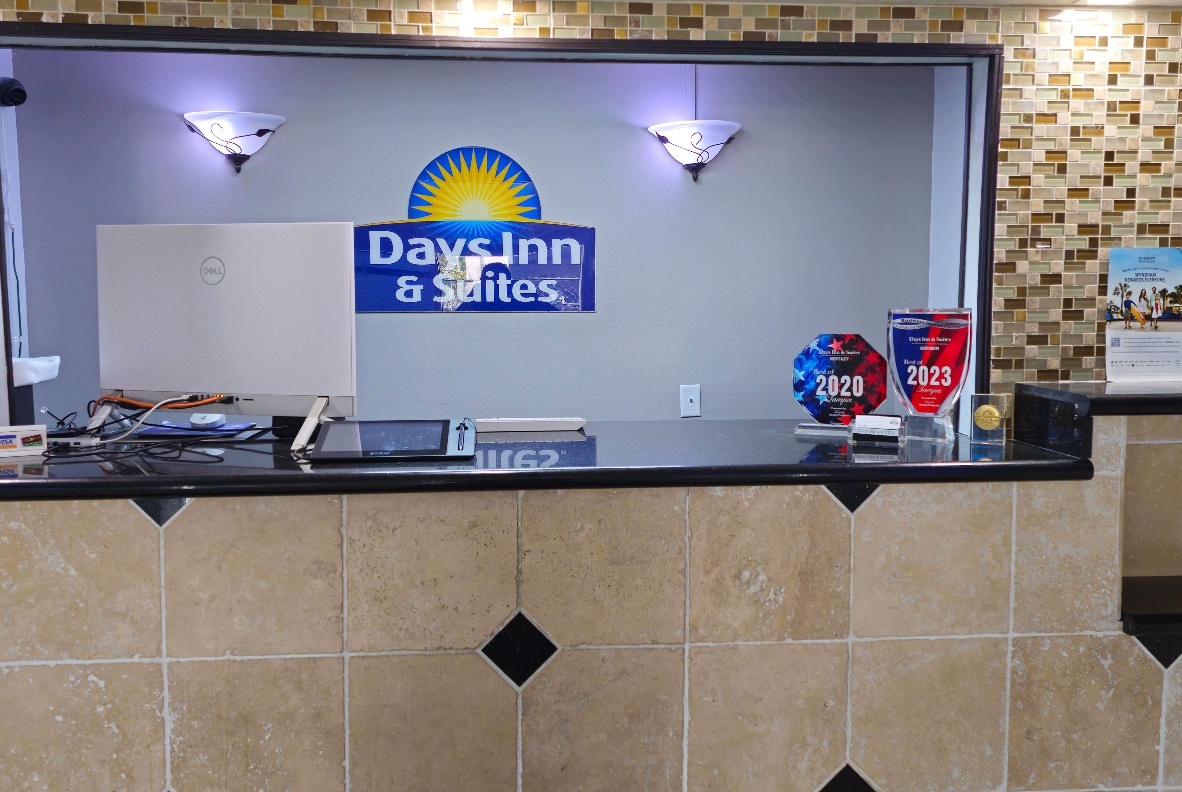 A reception desk with a sign for Days Inn & Suites, a computer, and a plaque for the Best of 2020 award.