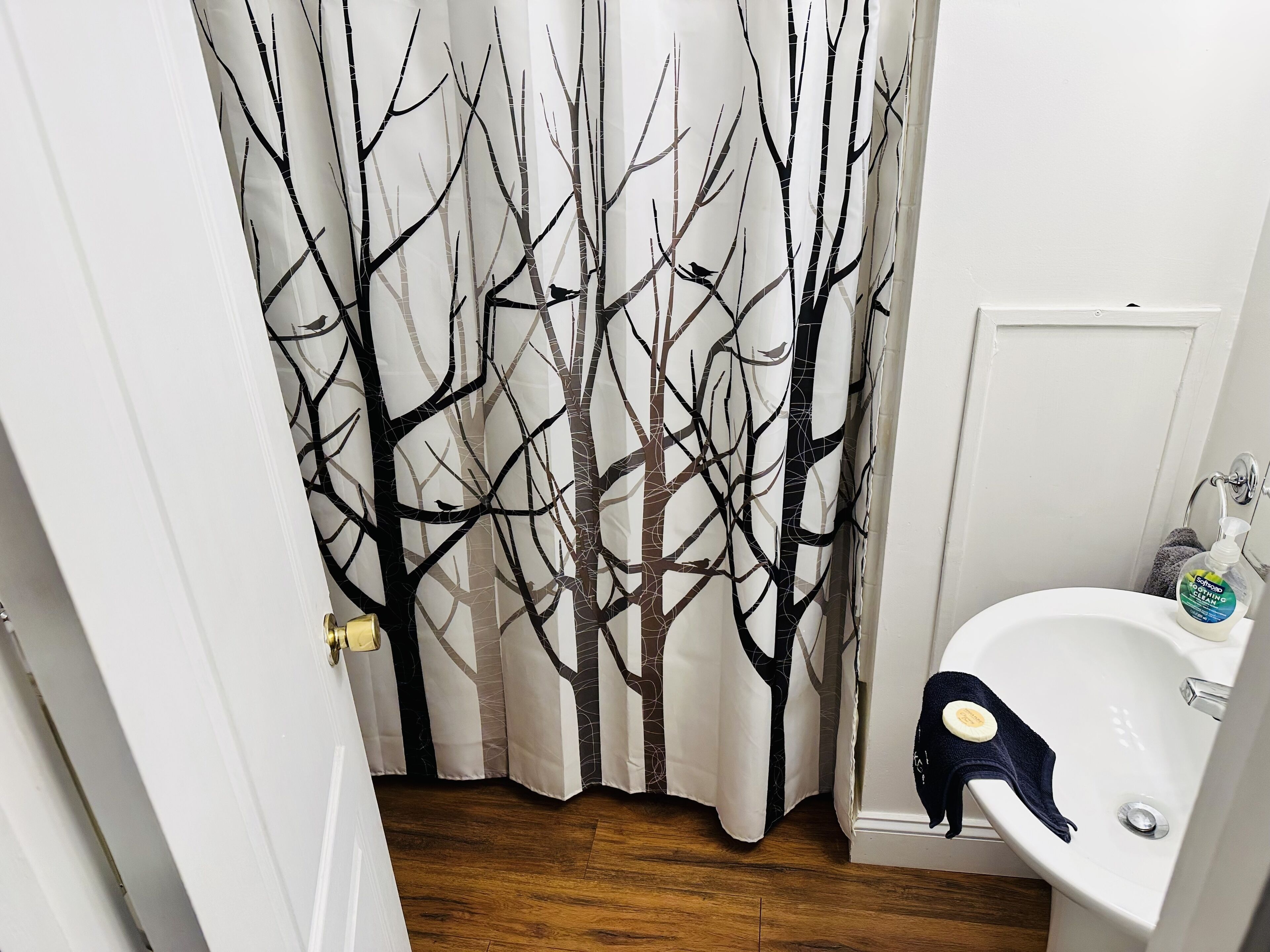 A bathroom with a white sink, a bottle of hand soap, and a towel hanging on the wall.