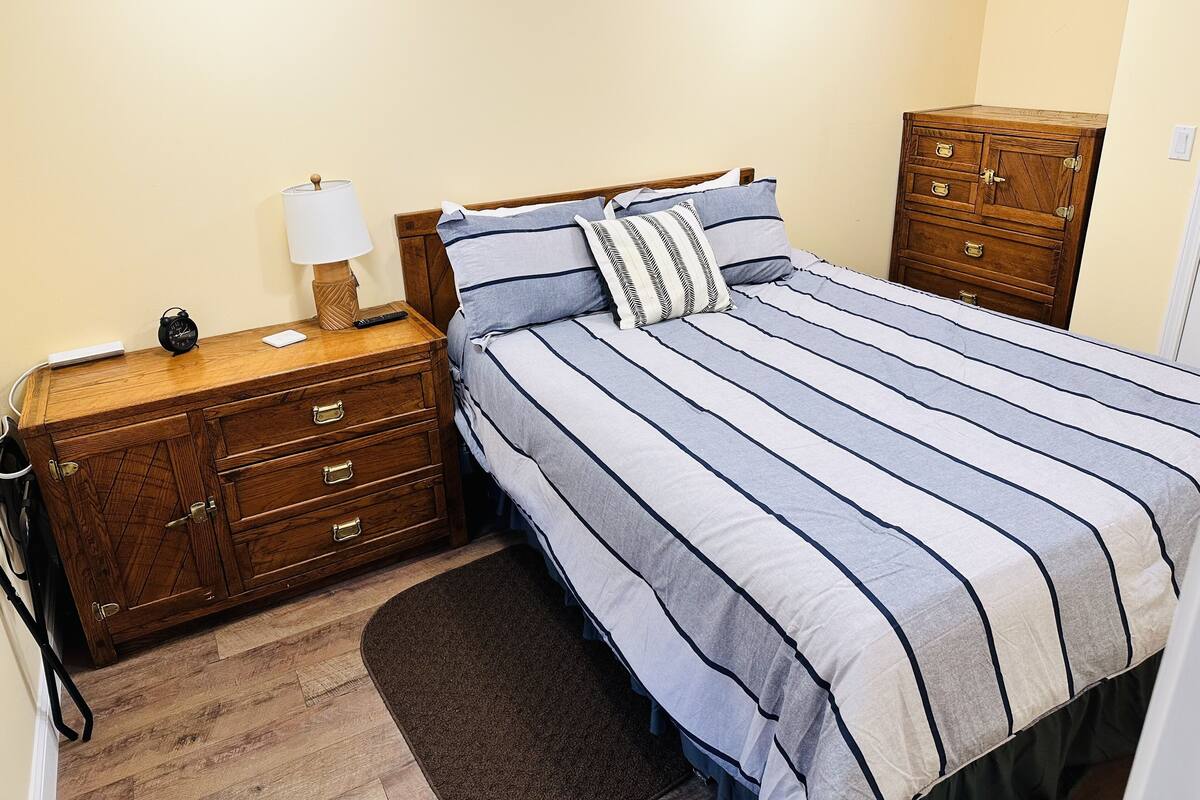A bedroom with a wooden nightstand, a lamp, a bed with striped bedding, and a wooden dresser.