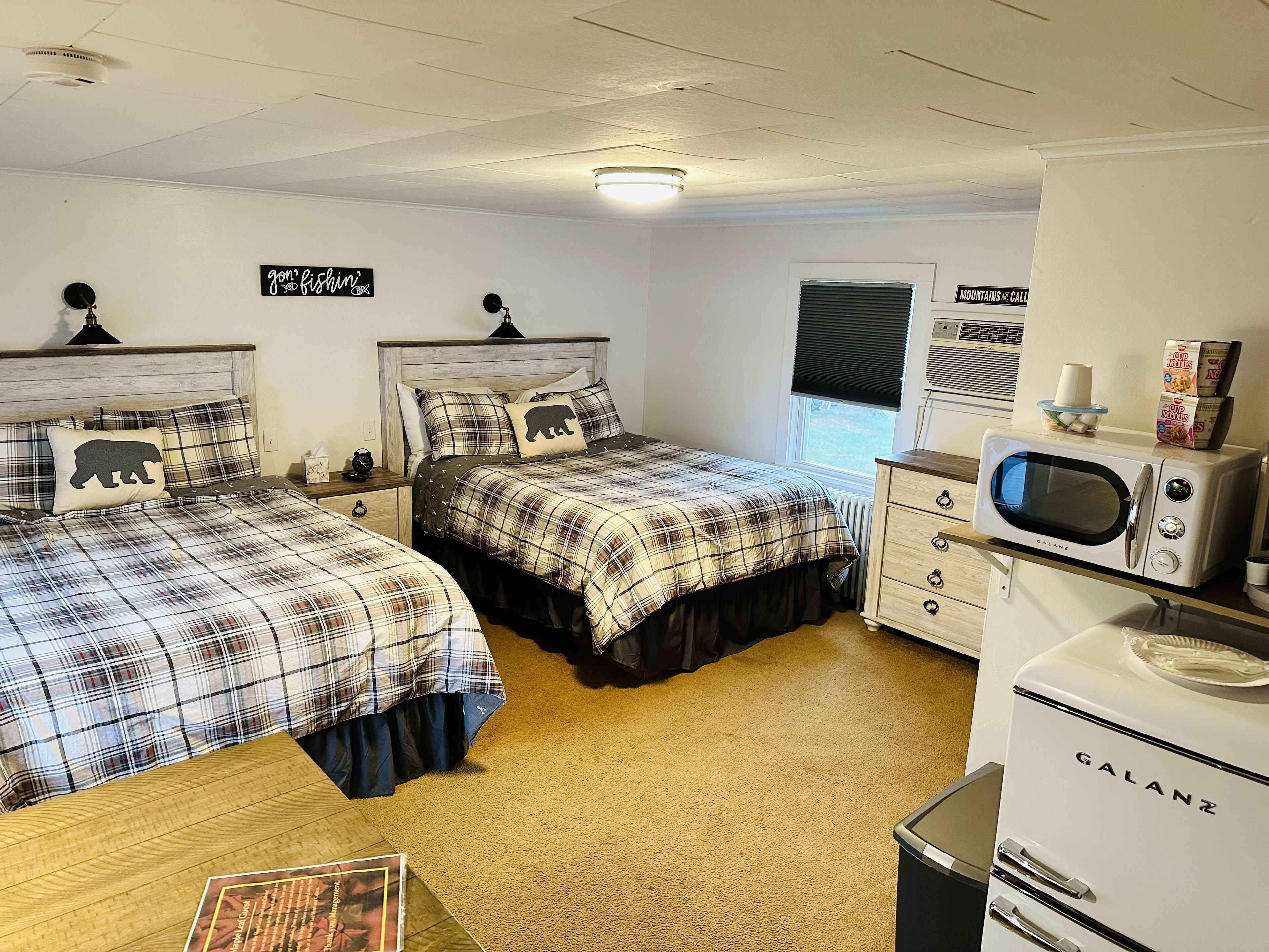 A bedroom with two beds, a kitchenette, and a window with blinds.
