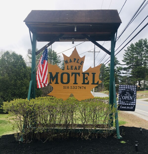A Maple Leaf Motel sign with an American flag, surrounded by greenery.