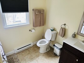 Un baño con inodoro, lavamanos, espejo, toallero y una ventana con persianas.