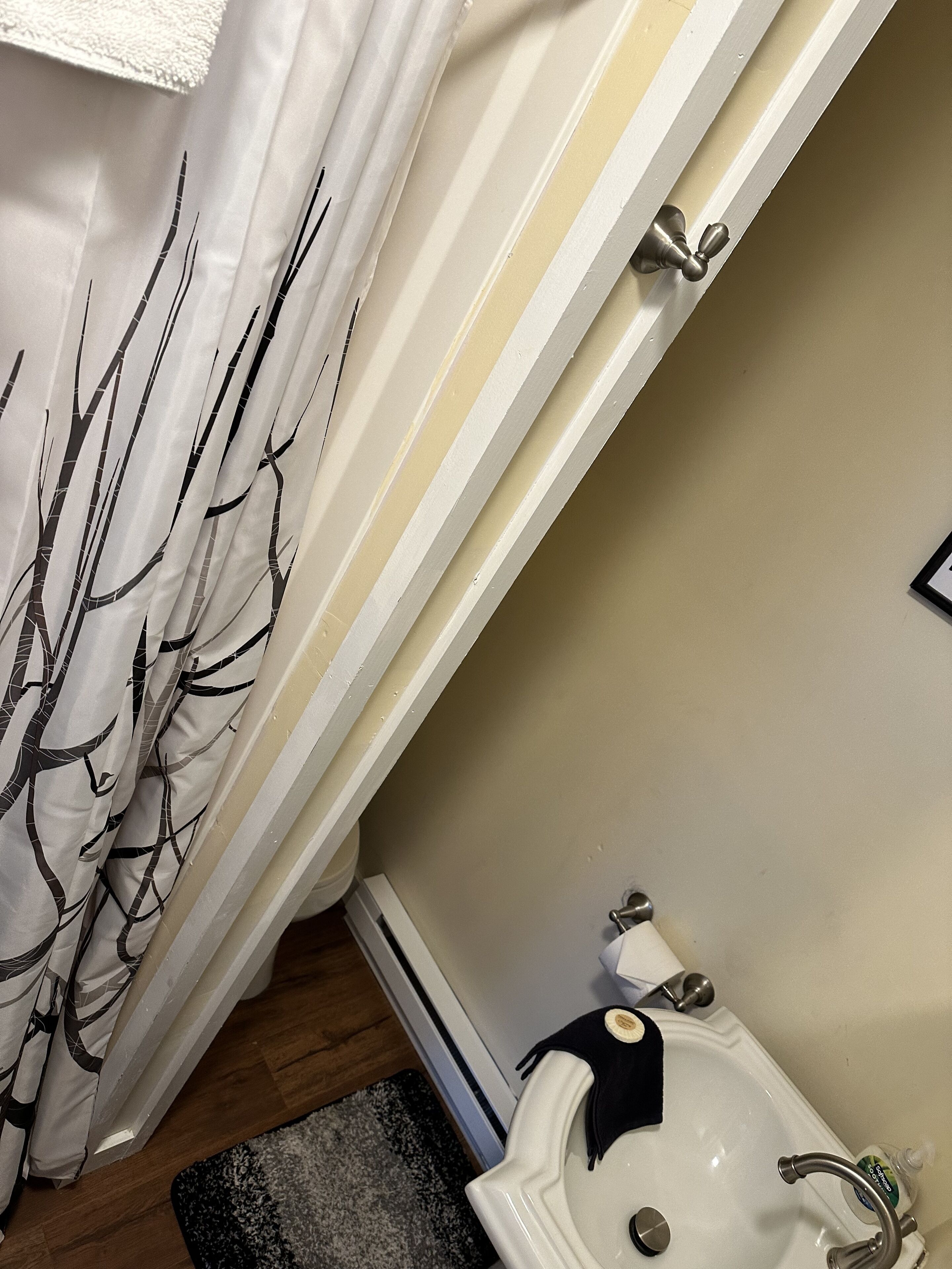 A bathroom with a white sink, a black towel, and a white shower curtain with a tree pattern.