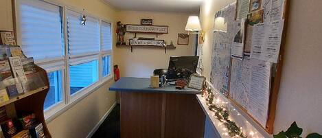 A small office with a desk, a bulletin board, and a window with blinds.
