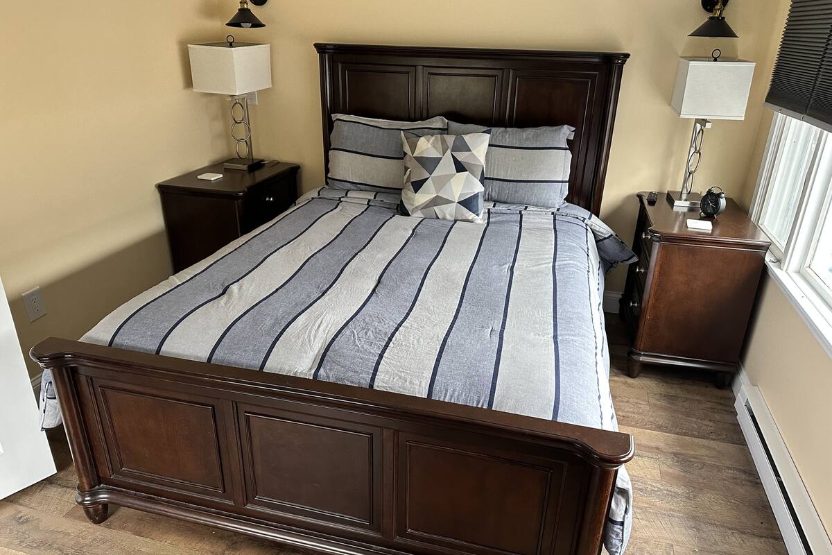 A bedroom with a large bed, two nightstands, and a window with blinds.