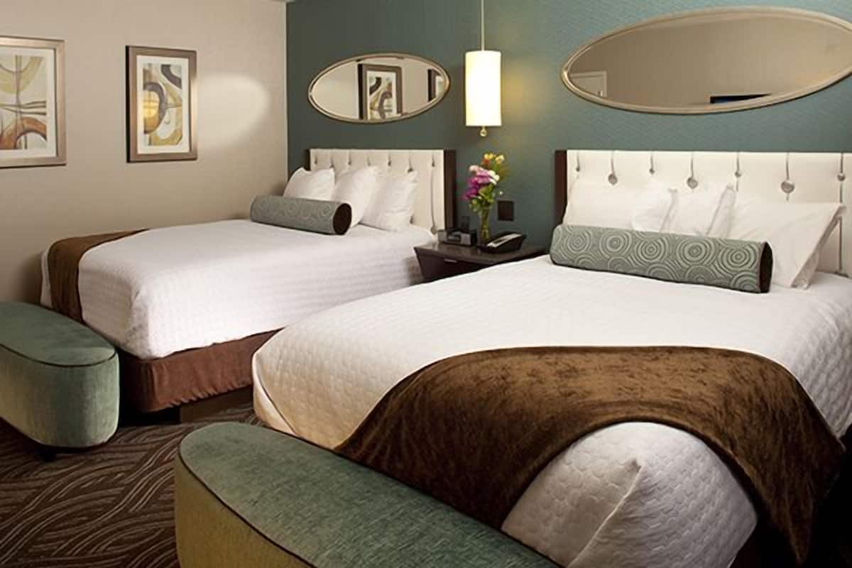 A hotel room with two beds, a bench, a nightstand with a lamp, and artwork on the walls.