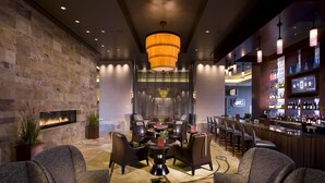 A modern lounge area with a fireplace, comfortable seating, a bar with a variety of bottles, and a large chandelier. - Northern Quest Resort And Casino (Airway Heights)