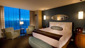 A hotel room with a large bed, two armchairs, a side table, a lamp, a mirror, and a view of the ocean. - Northern Quest Resort And Casino (Airway Heights)