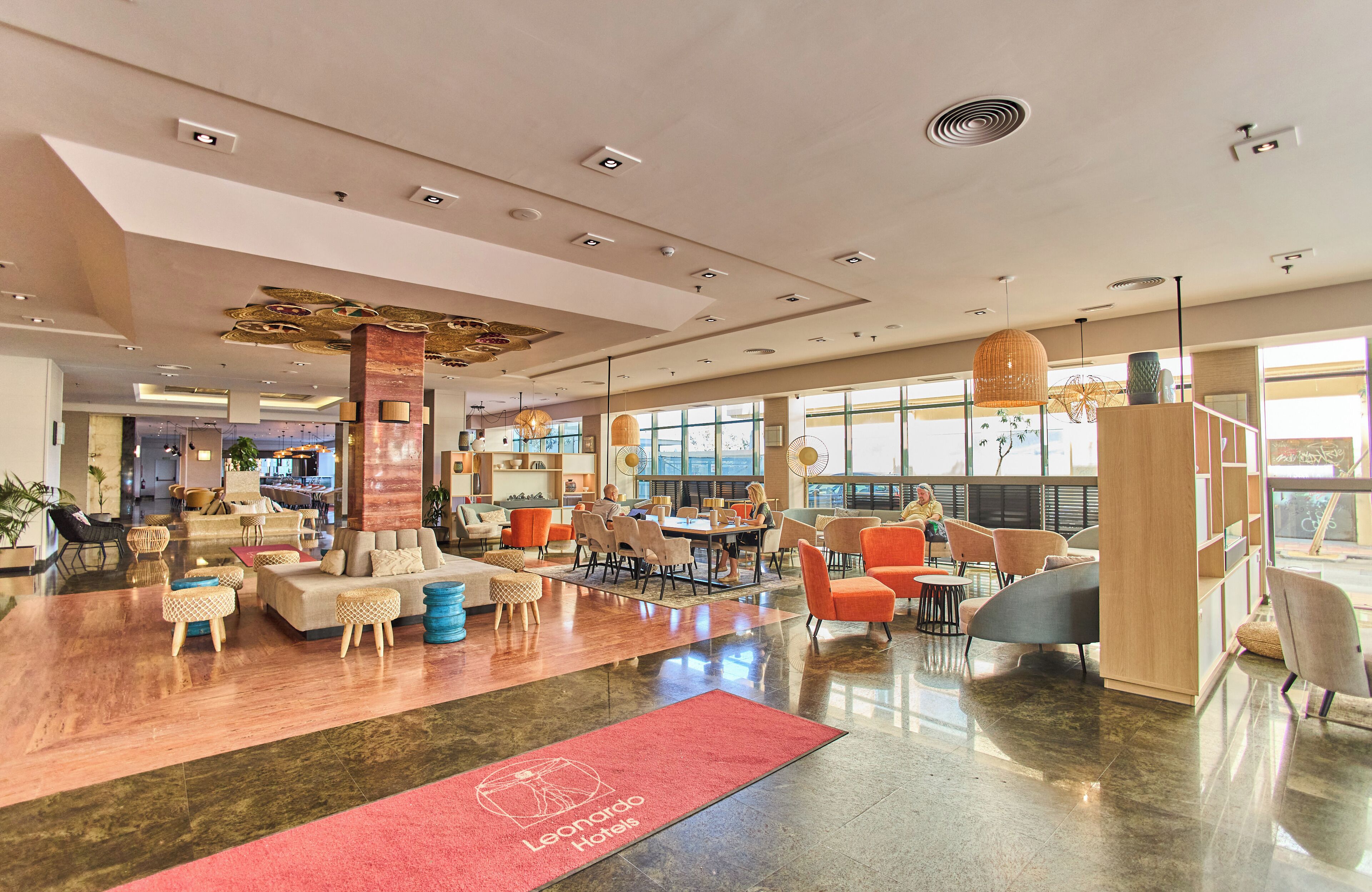A spacious hotel lobby with a red carpet, modern furniture, and large windows offering views.