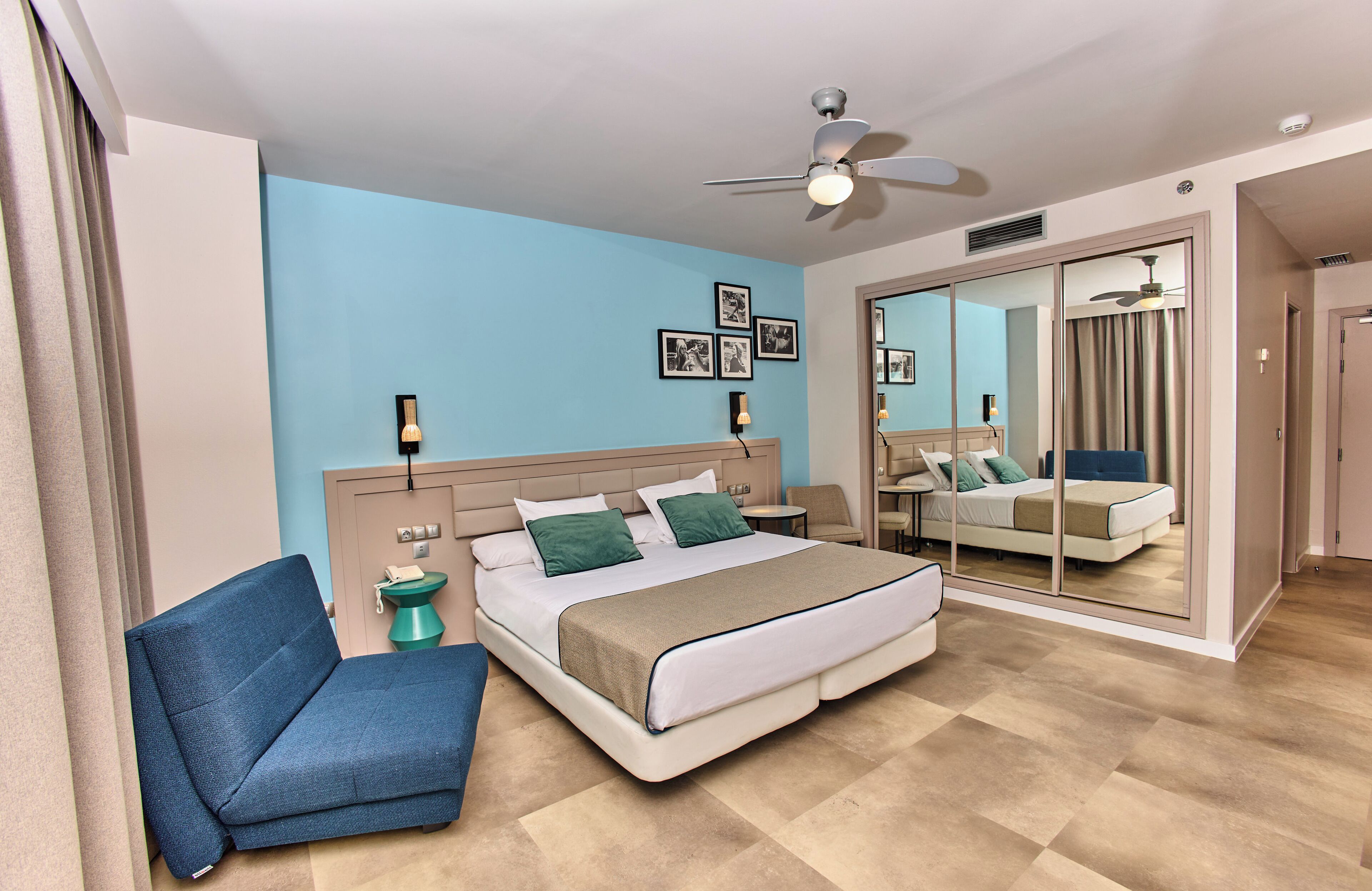 A modern hotel room with a bed, a chair, a bedside table, and a large mirror.