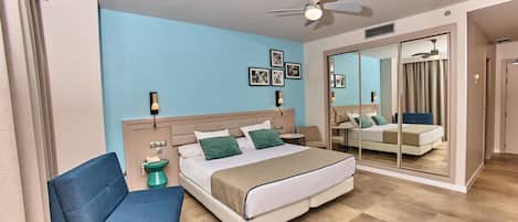 A modern hotel room with a bed, a chair, a bedside table, and a large mirror.