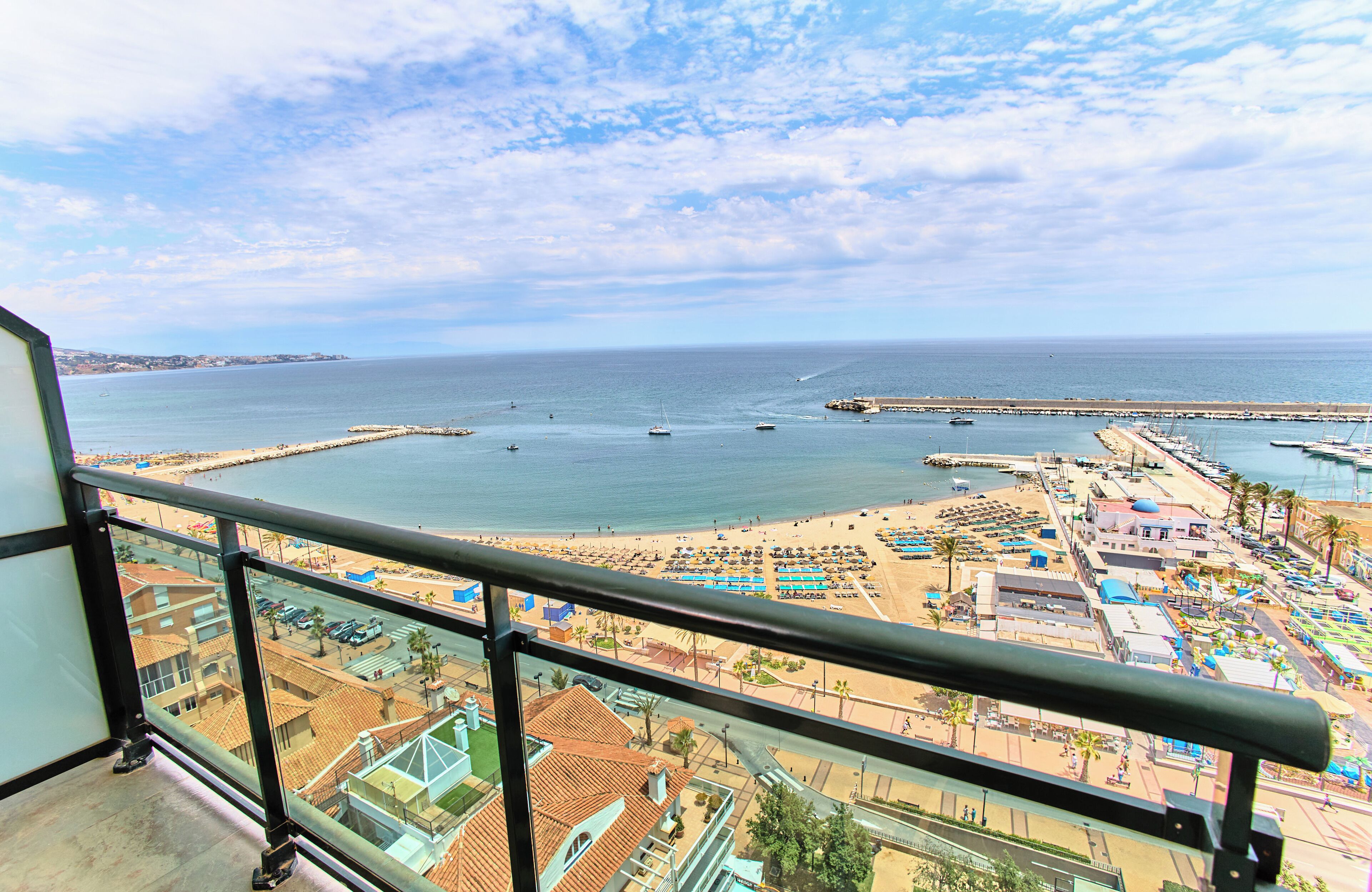 A coastal view from a balcony overlooking a beach, a marina, and adjacent buildings.