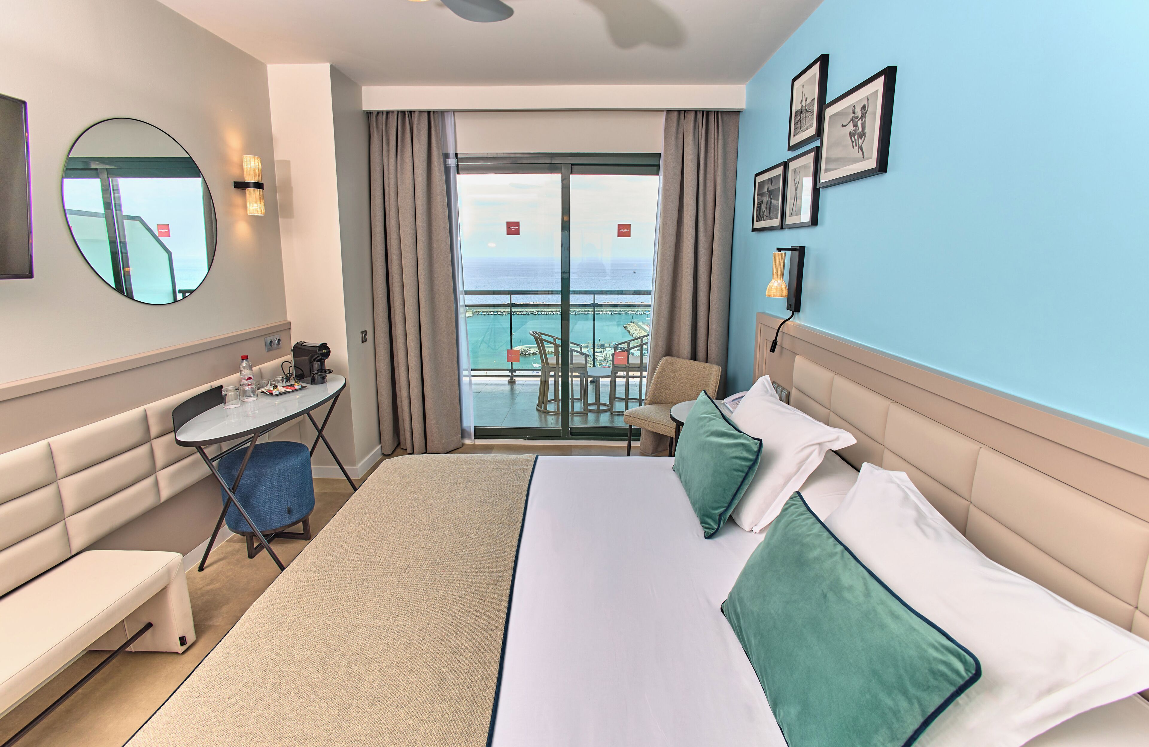 Een hotelkamer met een groot bed, een zithoek, een tafeltje en een balkon met uitzicht op zee.