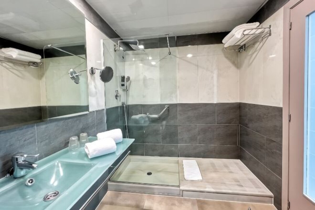 Un baño moderno con ducha envuelta en vidrio, un lavamanos con encimera de mármol y un espejo.