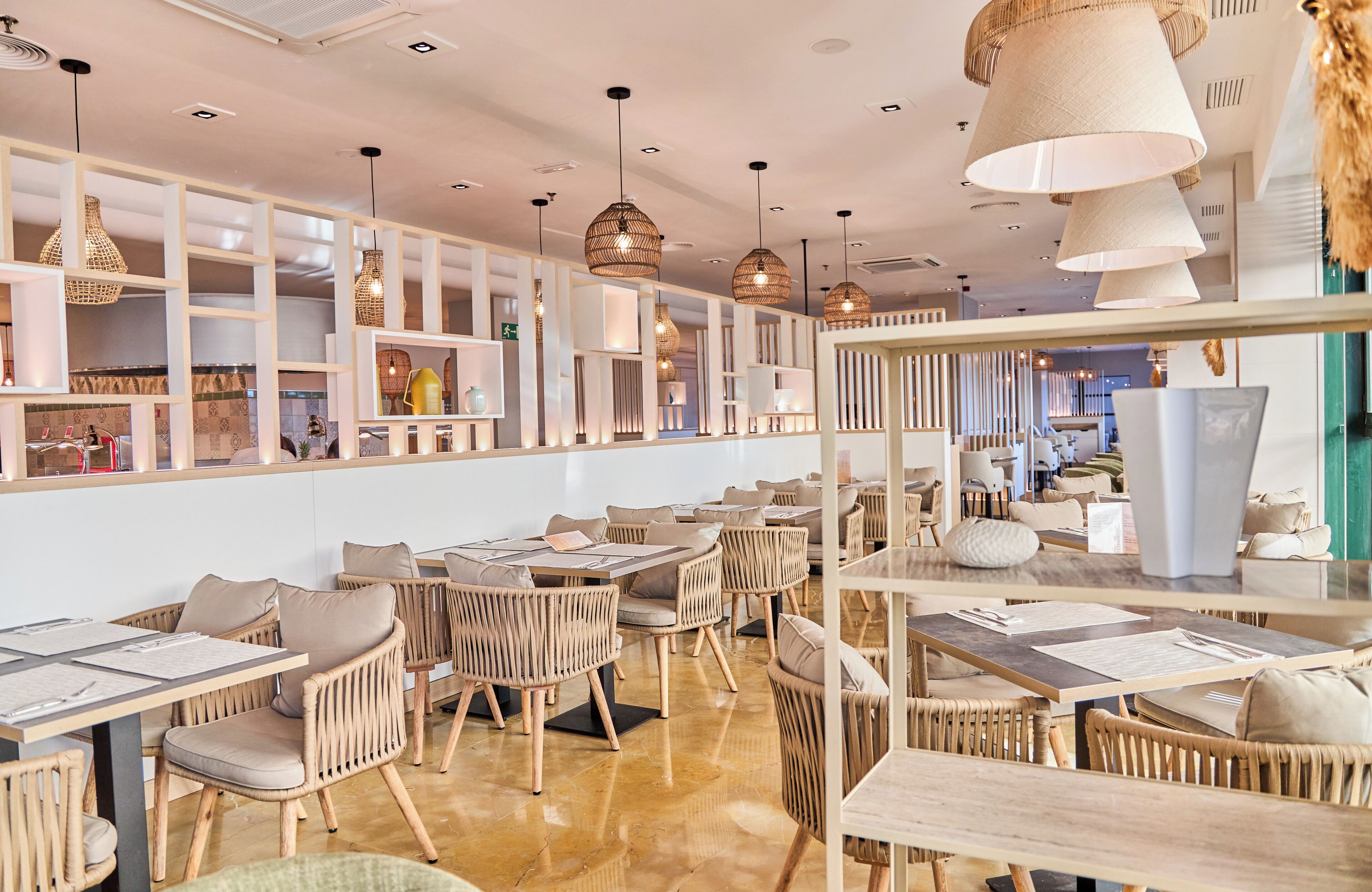 A modern restaurant interior with wicker furniture, pendant lighting, and a clean, organized layout.