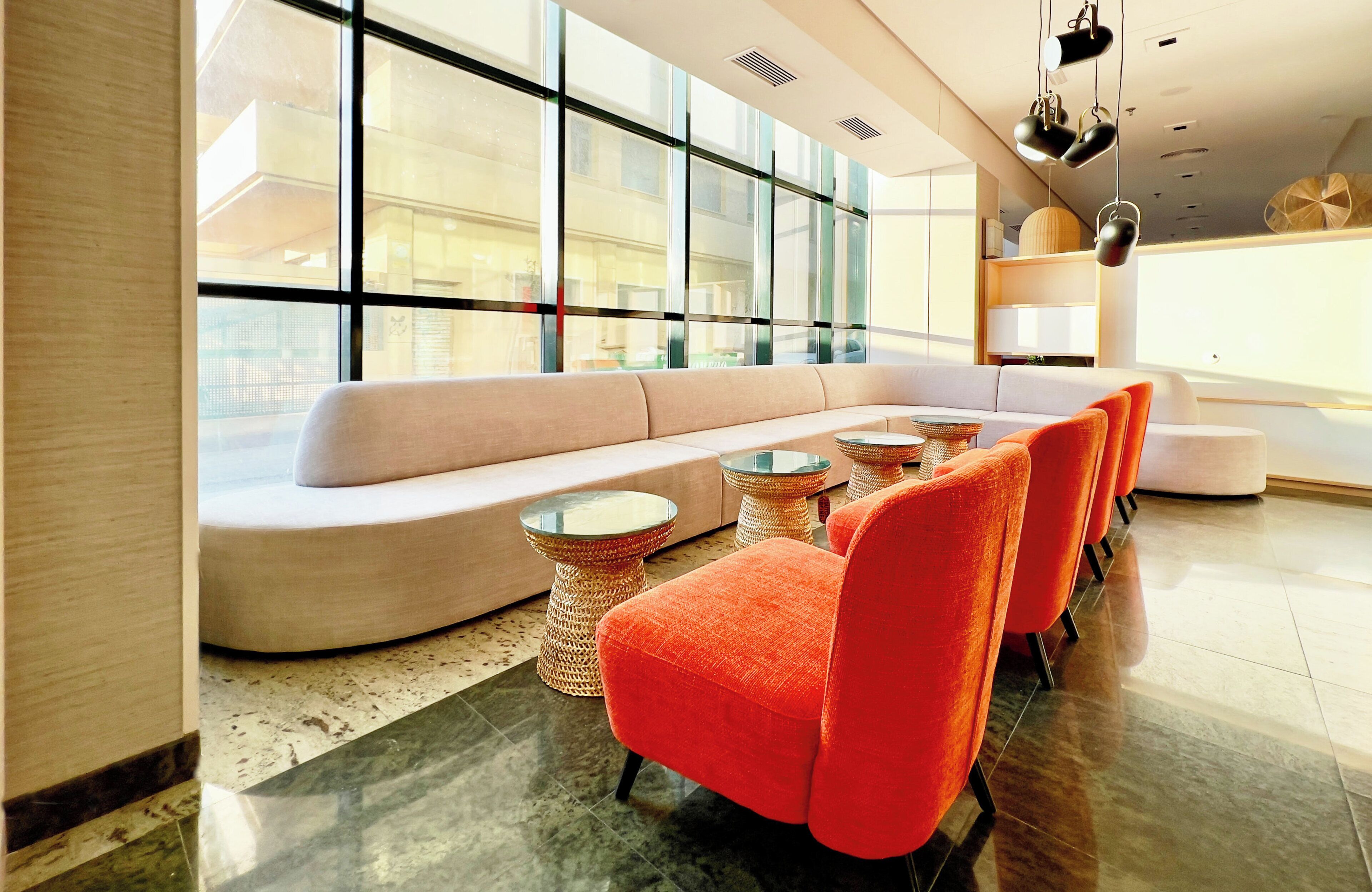 A modern lounge area with a curved sofa, orange armchairs, and round tables.