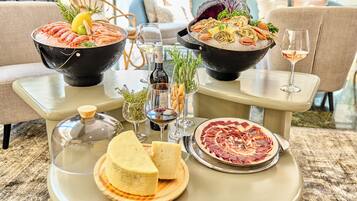 Une table à manger dressée avec des plats de fruits de mer, des verres à vin et des assiettes de fromage, dans une pièce bien éclairée où l’on aperçoit un canapé et des fauteuils au fond.
