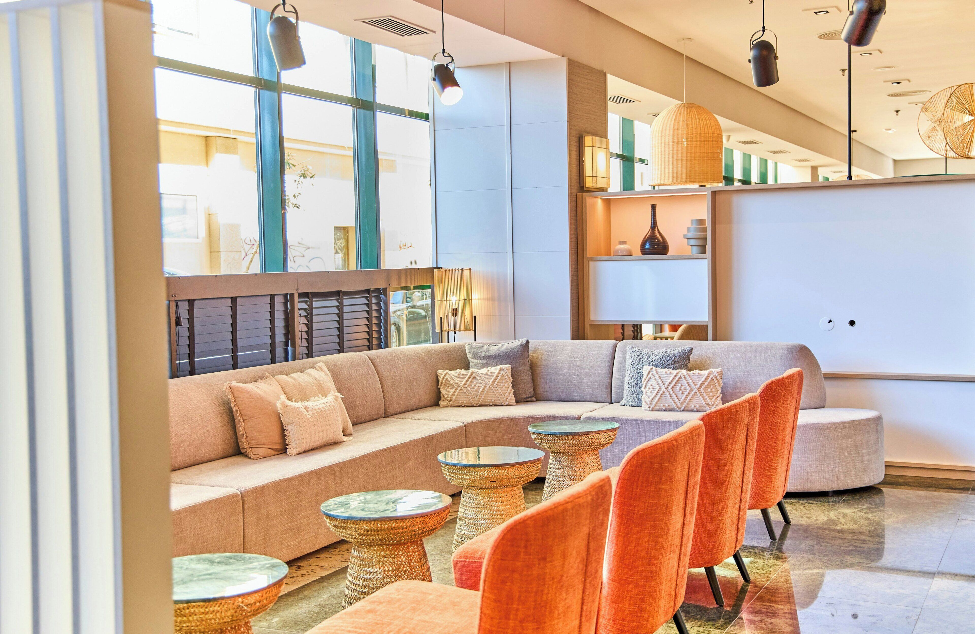 A modern lounge area with a sectional sofa, round tables, and orange chairs.