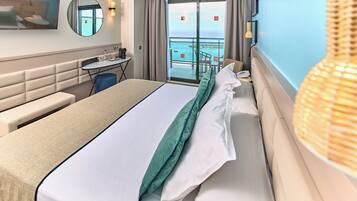 Ein Hotelzimmer mit einem großen Bett, einem Schreibtisch, einem Sessel, einem kleinen Tisch, einem Spiegel und Meerblick durch eine Schiebetür.
