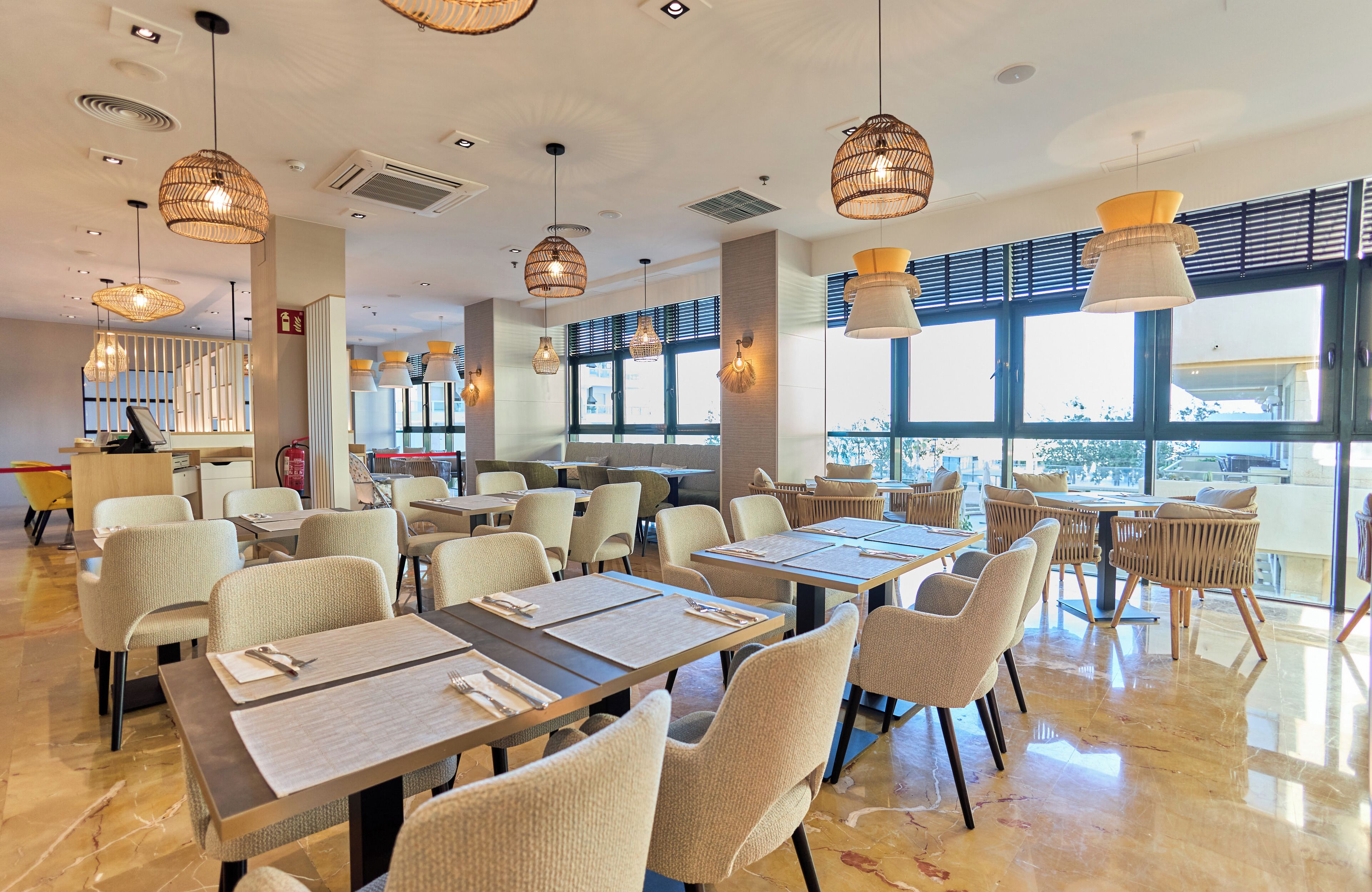 A spacious restaurant with high ceilings, modern pendant lighting, and large windows offering a view of the city.