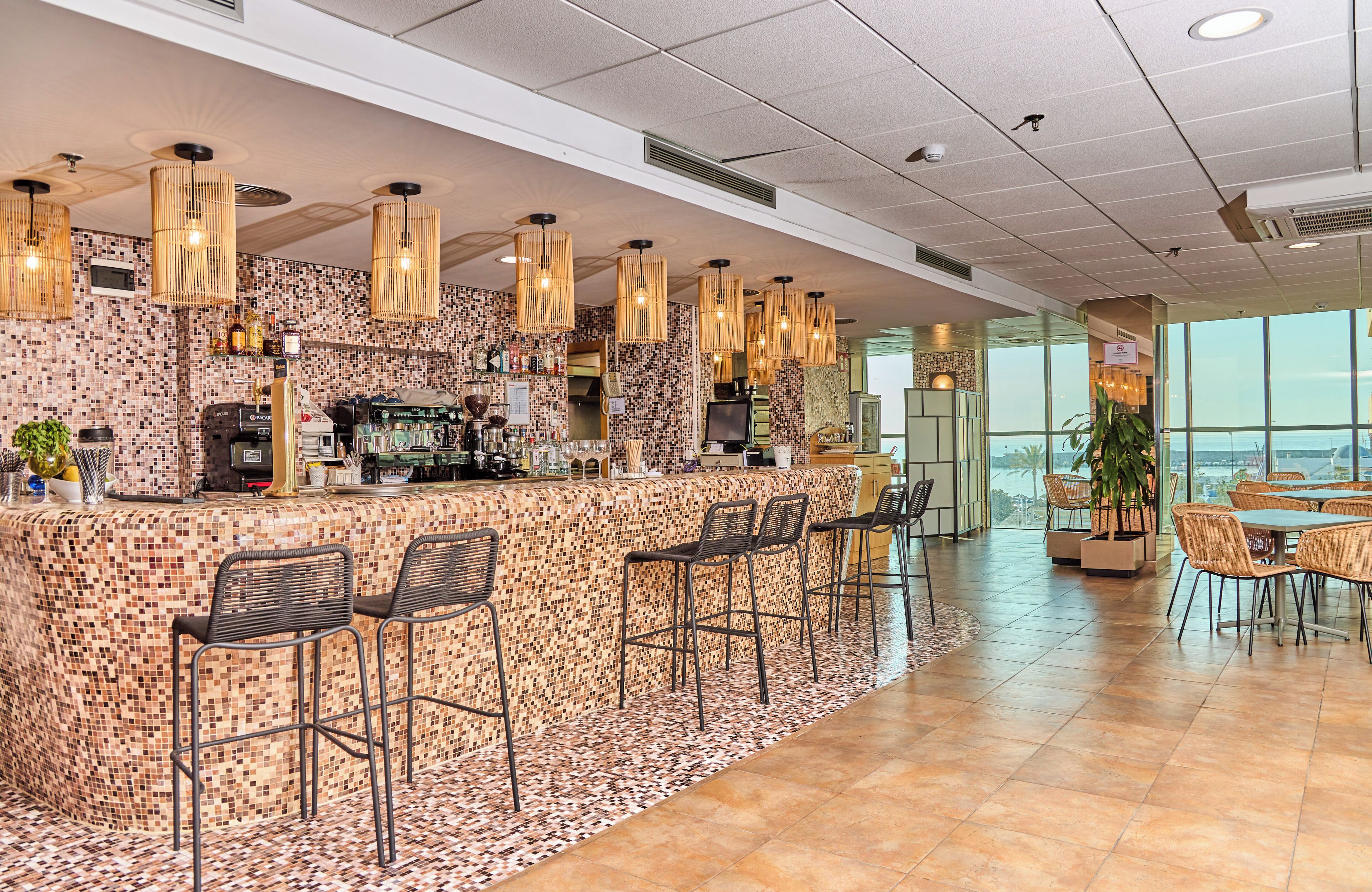 Un espace bar agrémenté d’un mur recouvert de mosaïques, de tabourets de bar et de luminaires suspendus.