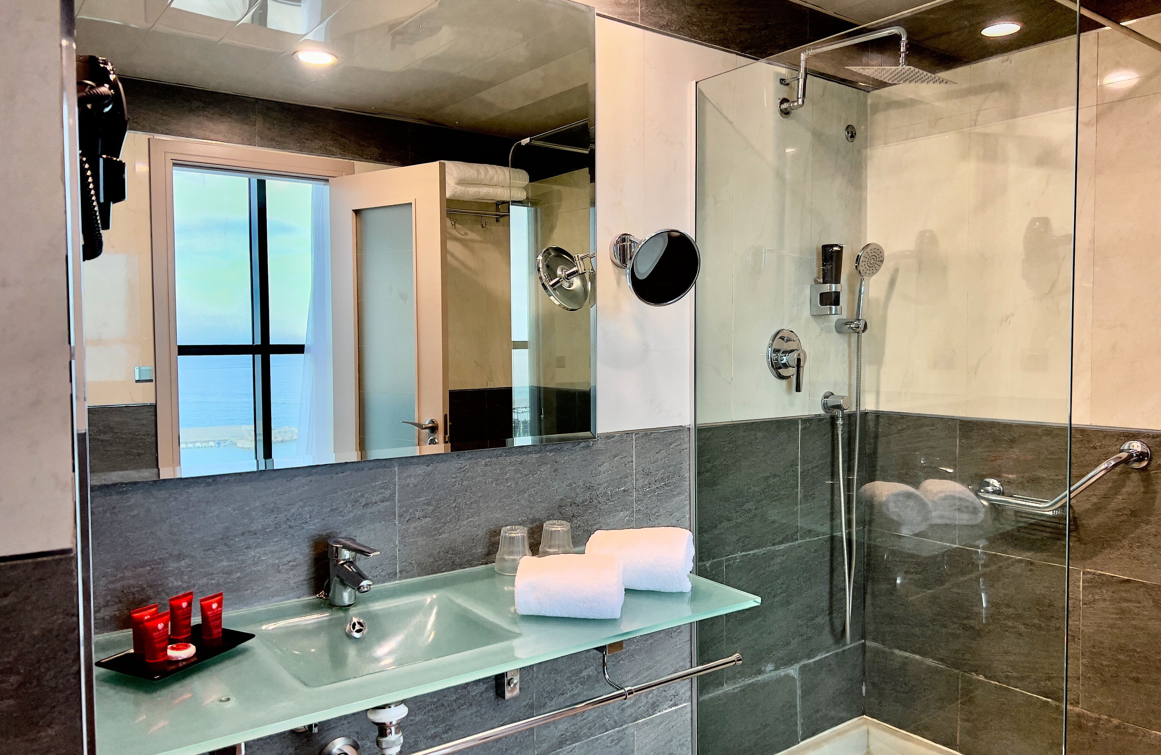Un baño moderno con cabina de ducha de vidrio, lavamanos de vidrio y un espejo grande.