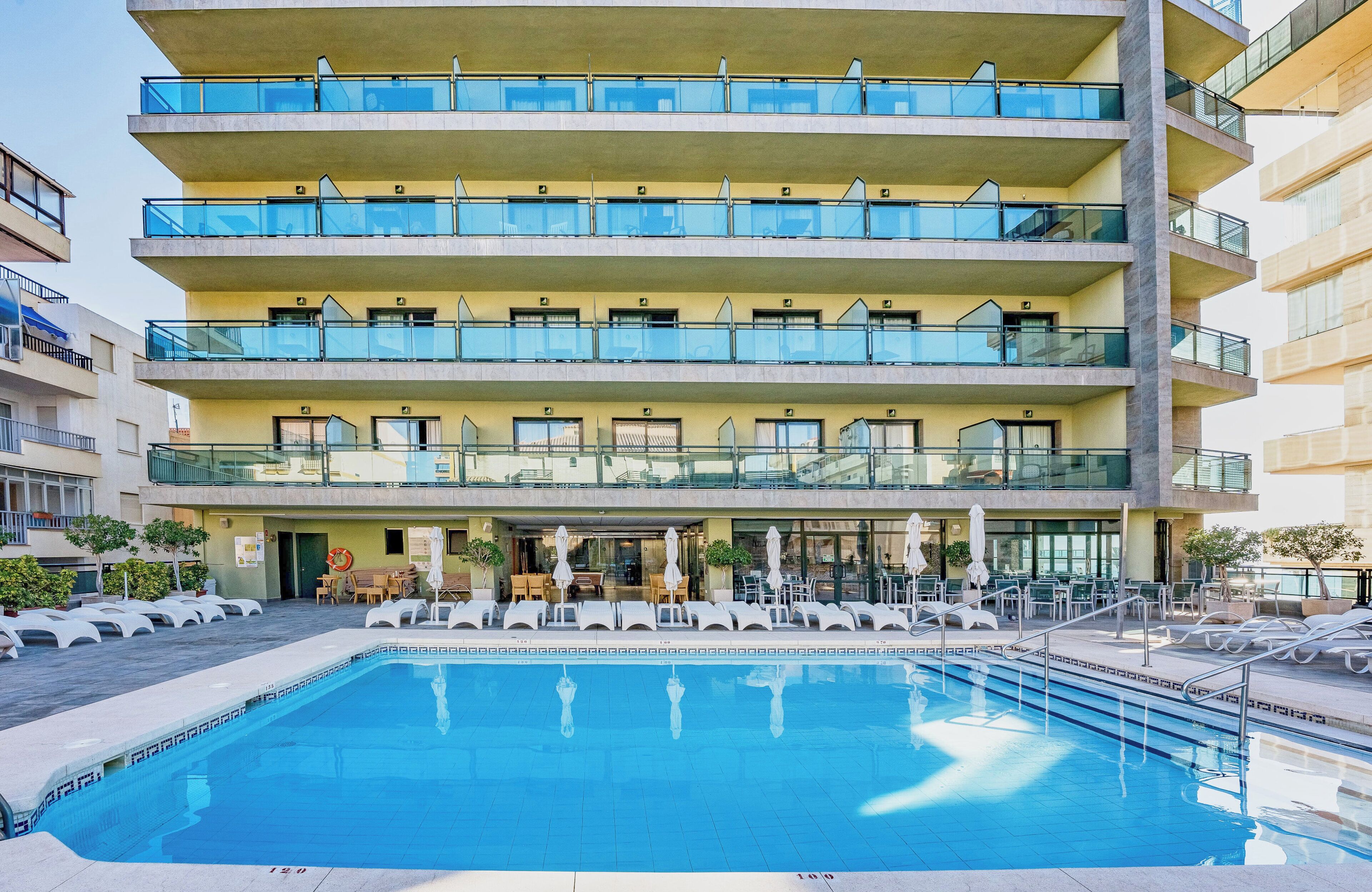 Ein mehrstöckiges Hotel mit Schwimmbad, Sitzgelegenheiten im Freien und Balkonen.