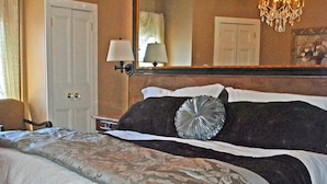 Een slaapkamer met een groot bed, een kroonluchter, een spiegel en een deur.