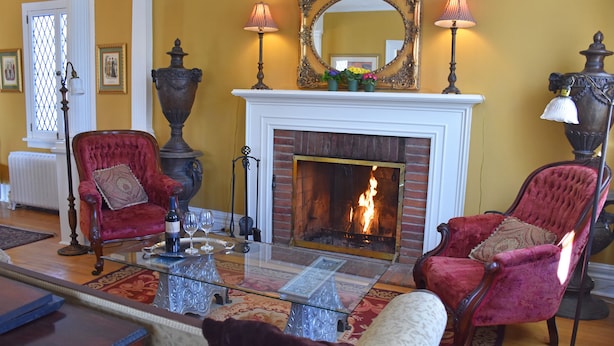 Een woonkamer met een open haard, twee rode fluwelen fauteuils, een glazen salontafel en een spiegel boven de haard.