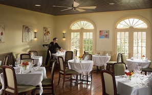 A dining area with round tables, chairs, and artwork on the walls. - Inner Banks Inn (Edenton)