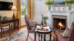 A cozy living room with a fireplace, comfortable seating, a television, and a dining table with a fruit platter.