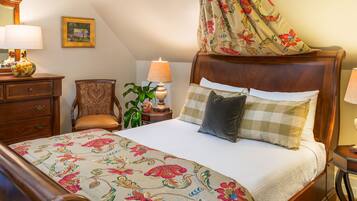 A bedroom with a wooden bed, floral bedspread, a chair, a nightstand with lamps, and a painting on the wall.
