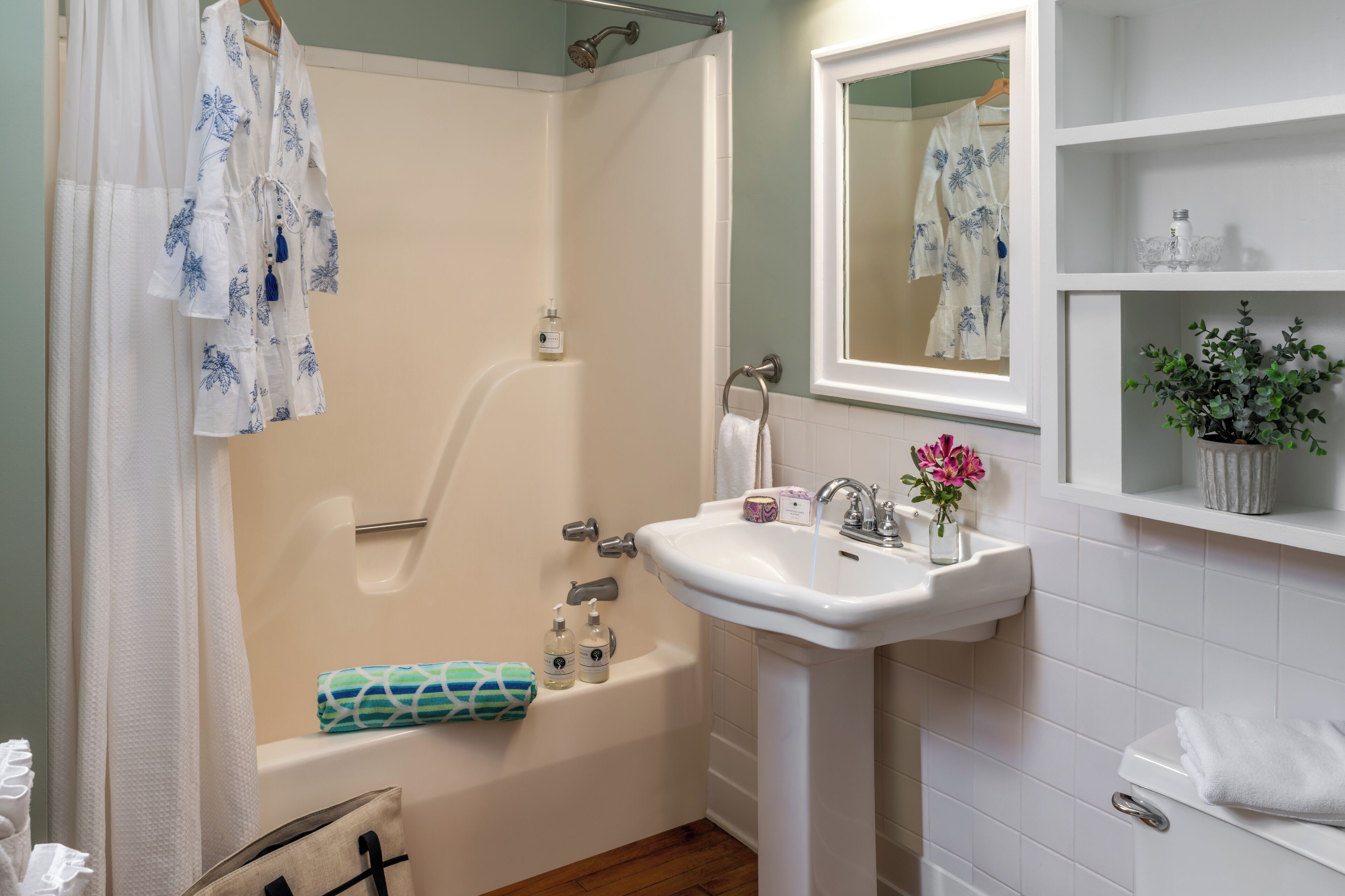 Une salle de bain équipée d’une baignoire, d’un lavabo, d’un miroir et d’une étagère contenant des articles de toilette.