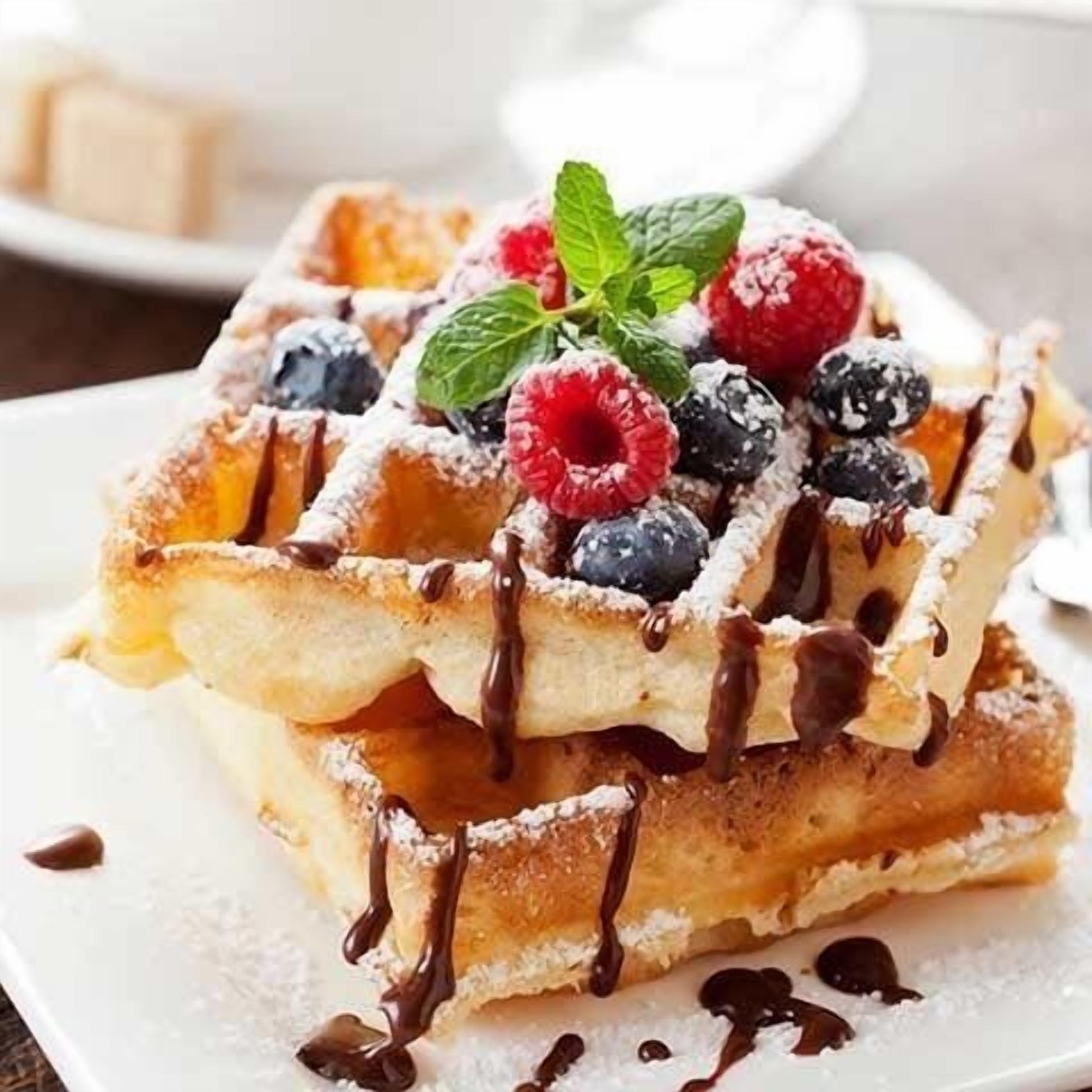 A stack of waffles topped with chocolate syrup, fresh berries, and a mint leaf.