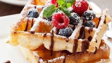 A stack of waffles topped with chocolate syrup, fresh berries, and a mint leaf.