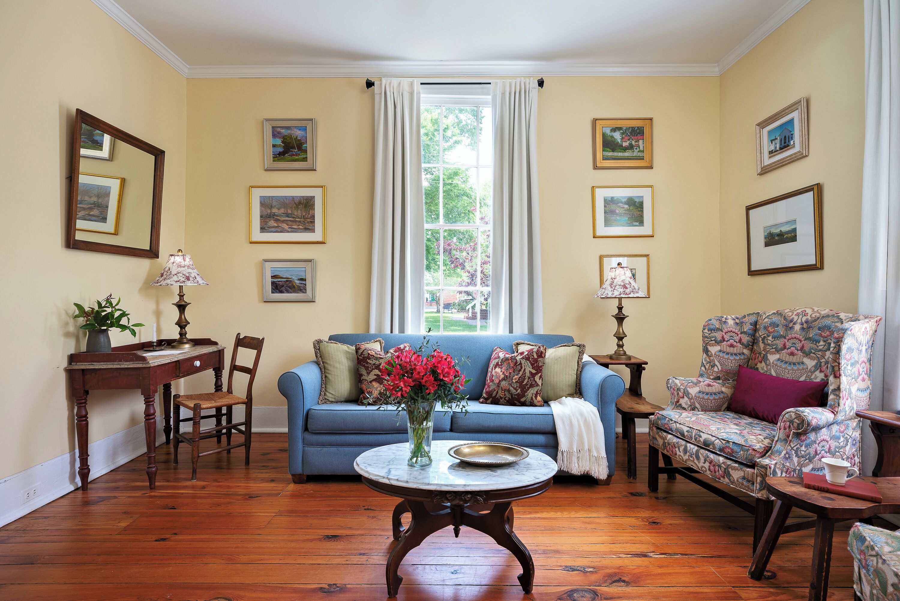 A living room with a blue sofa, floral armchair, wooden coffee table, and framed pictures on the walls.