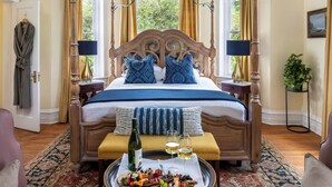 A bedroom with a four-poster bed, a tray with snacks and drinks, and a view of greenery outside. - Inner Banks Inn (Edenton)