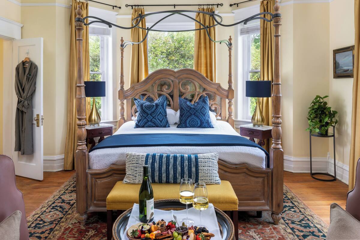 Quarto com cama de dossel, bandeja com petiscos e bebidas, e vista para o verde lá fora.