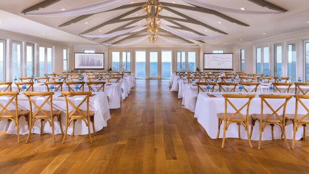 A conference room with tables set for a meeting, large windows, and a view of the sea. - Inner Banks Inn (Edenton)