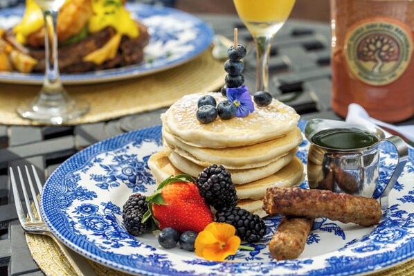 A breakfast plate with pancakes, berries, sausage, and a glass of juice.