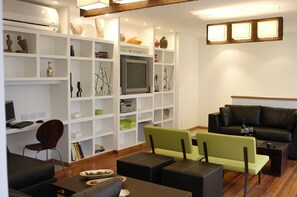 Un salon moderne doté d’un téléviseur à écran plat, d’un canapé, d’une table basse et d’une bibliothèque remplie d’objets décoratifs.