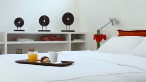 A neatly made bed with white linens, a tray with breakfast items, a bedside table with a lamp, and a wall with decorative items and a shelf. - Didi Rooms (Buenos Aires)