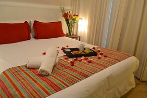 Un lit bien fait, recouvert d’une courtepointe rayée aux couleurs vives, avec des oreillers rouges et un plateau contenant des articles pour le petit-déjeuner.