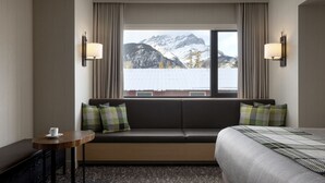 A hotel room with a bed, a sofa, a small table, and a window with a mountain view. - Peaks Hotel & Suites (Banff)