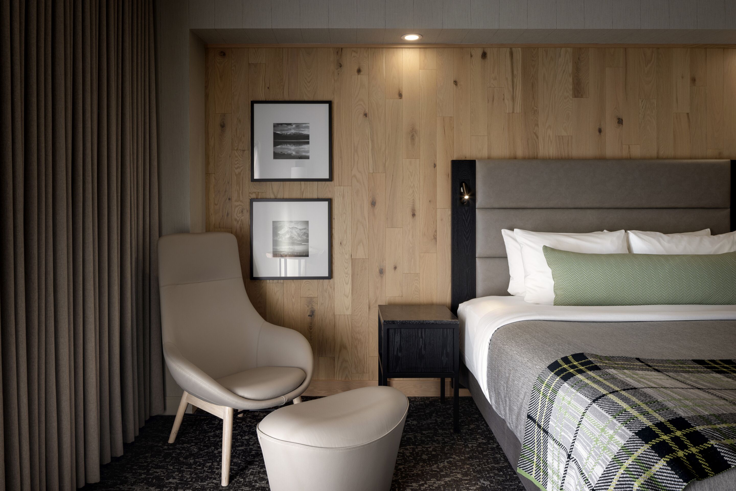 Habitación de hotel con una cama, una silla, una mesita y dos cuadros en la pared.