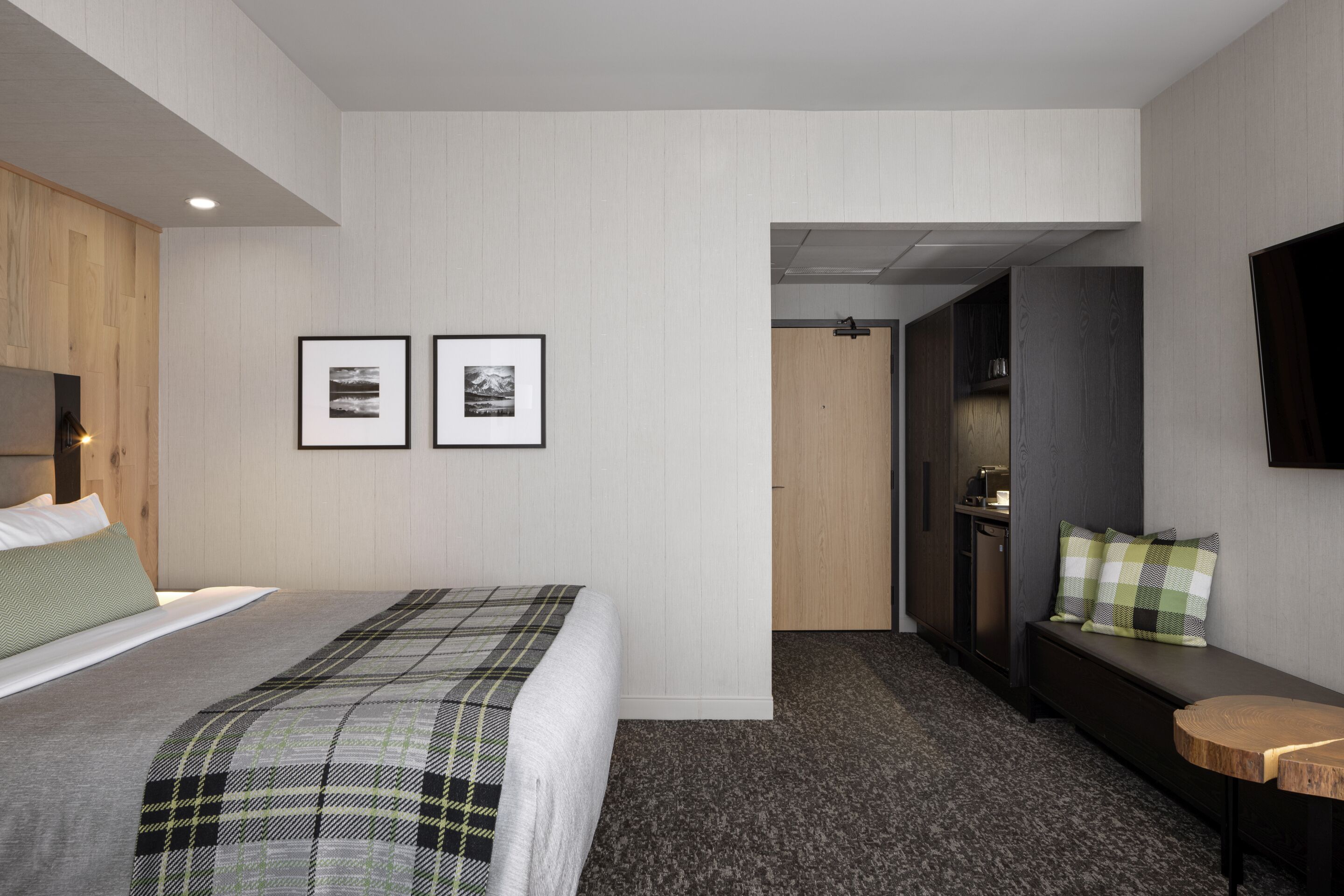 Une chambre d’hôtel moderne équipée d’un lit, d’une banquette, d’une petite table et d’un téléviseur fixé au mur.