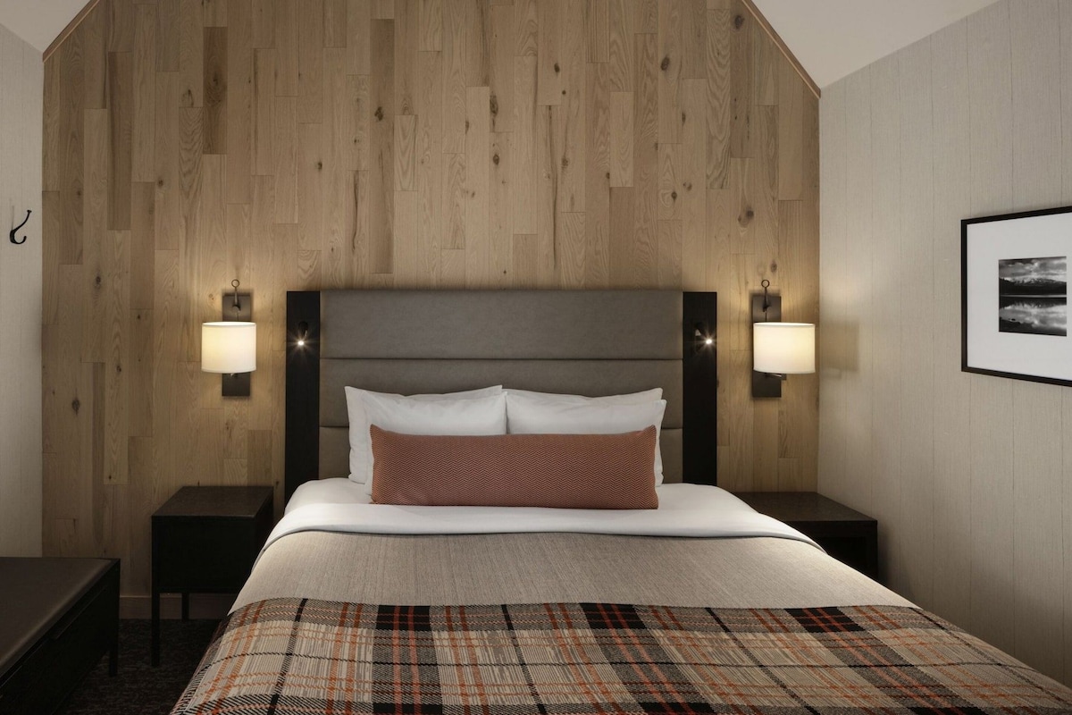 A hotel room with a large bed, two bedside tables, a headboard, and wall-mounted lamps.